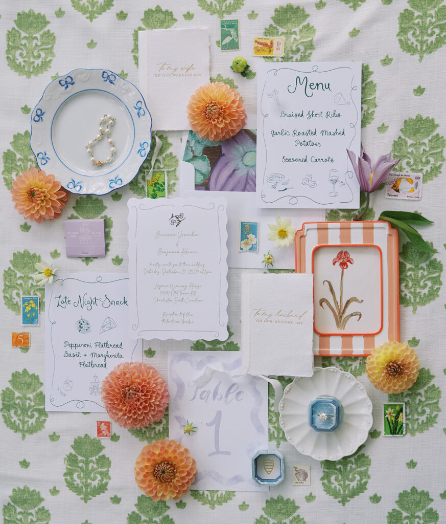 A whimsical wedding invitation suite and wedding day paper featuring greens, oranges, and purples styled with florals, vintage stamps and the bride's wedding jewelry.