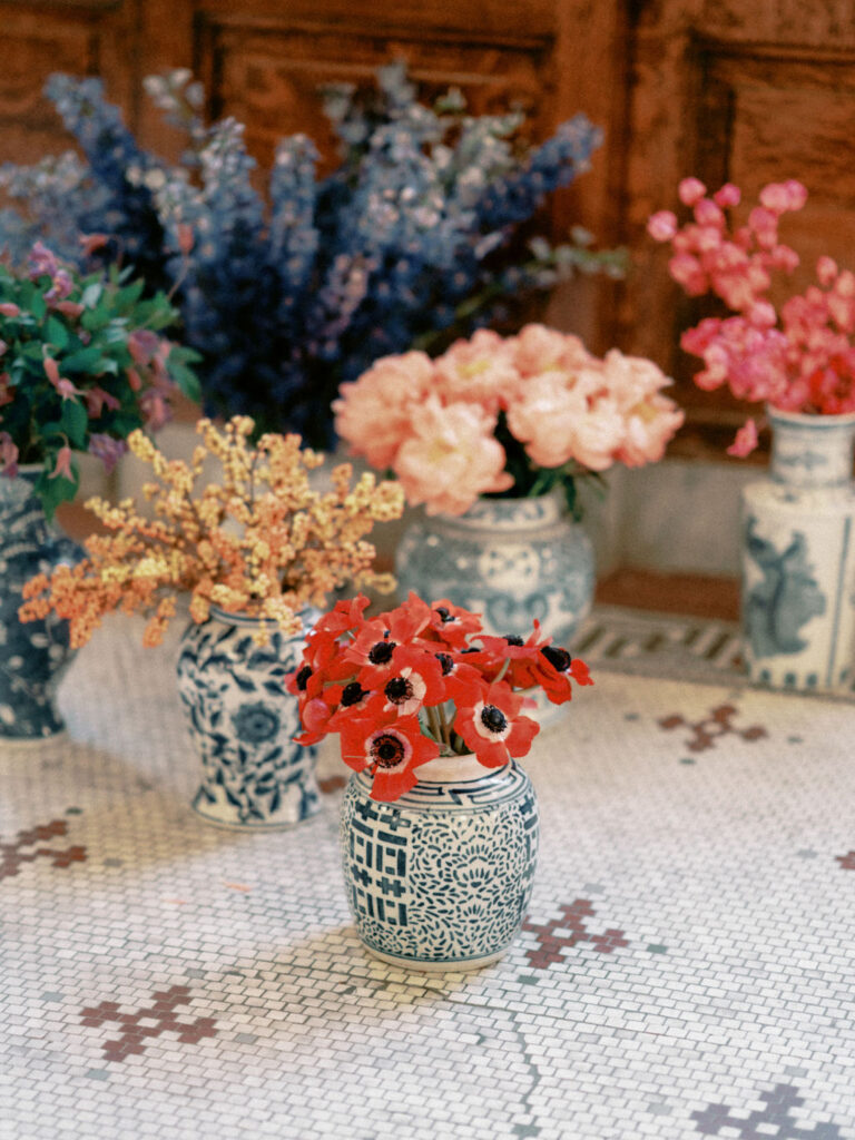 Monobloom arrangements in blue willow chinoiserie urns with pink peonies, red anemones, and blue delphinium.