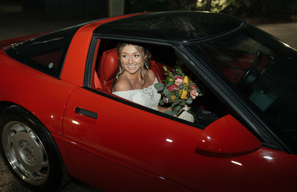 A bride and groom leaving their wedding reception in a red corvette.