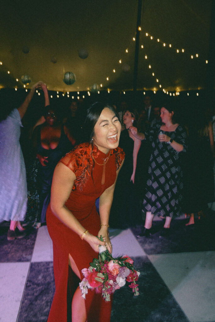 A smiling bride wearing a traditional red dress holding a red and pink floral floral bouquet.