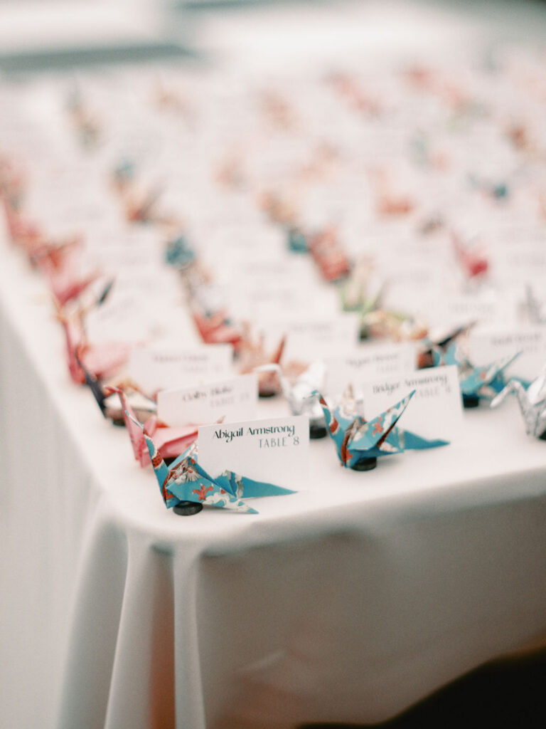 An escort card table featuring origami paper cranes made with colorful patterned papers with white cards reading the couple's names and table numbers.
