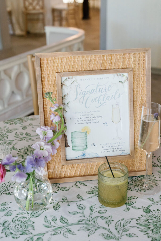 Rattan photo frame featuring watercolor illustrations of two signature cocktails: lavender prosecco and gold rush with the cocktails in their glasses in the foreground.