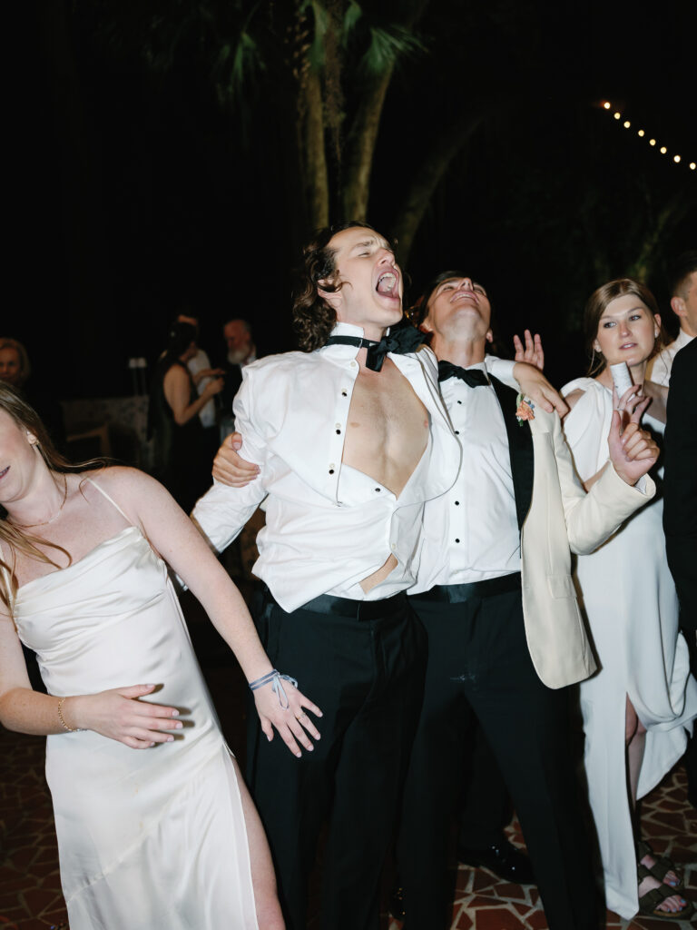 Guests dancing a wedding reception with a groomsmen singing in the center with his shirt unbuttoned.