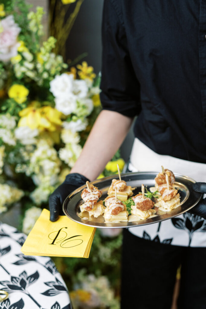 A server wearing a custom apron holding a silver tray of hors d'oeuvres and yellow napkins featuring the couple's monogram utilized in all of their wedding stationery.